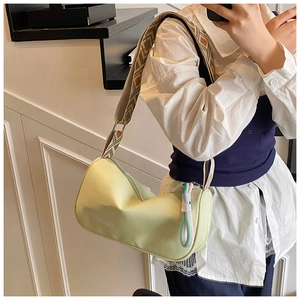 Détail d'un sac cylindrique vert clair avec bandoulière à motifs et pendentif décoratif