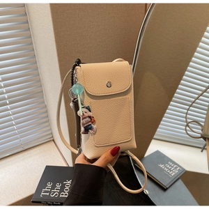 Détail du sac de téléphone beige en cuir grainé avec d'adorables breloques cartoon
