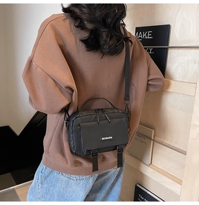 Detail of black crossbody bag with double zippers and buckle flap on model