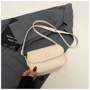 Detail of a creamy white crossbody bag showing lychee pattern texture and silver buckle