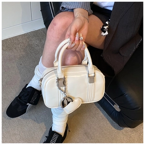 Detail of off-white bowling bag with double handles and a silver heart pendant chain