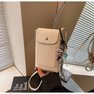 Gros plan du sac de téléphone blanc cassé à texture litchi avec breloques chien et sucette