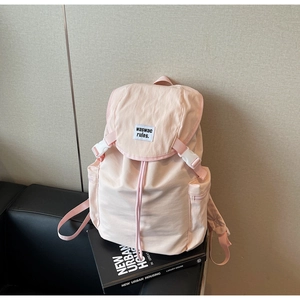 Detail of pink canvas backpack showing buckle flap, woven label and side zipper pocket