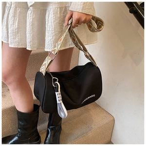 Détail du sac cylindrique noir avec bandoulière géométrique et broderie de lettres