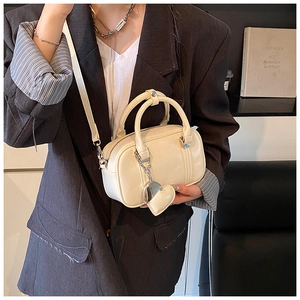 Detail view of cream Boston bag featuring a heart pendant and slim cross-body strap