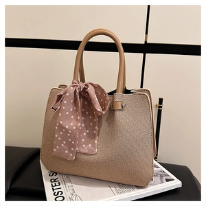 Détail du sac à main en paille tressé avec anses en cuir marron et foulard à pois roses