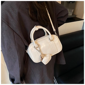 Detail of cream glossy mini Boston bag with heart charm and detachable shoulder strap