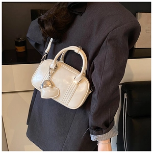 Close-up of cream Boston bag in patent leather with heart charm and seam detail