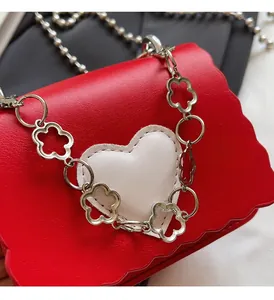 Detail of red mini shoulder bag featuring a white heart patch and silver flower chain