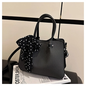 Détail d'un sac seau noir avec foulard à pois sur la poignée et bandoulière en cuir