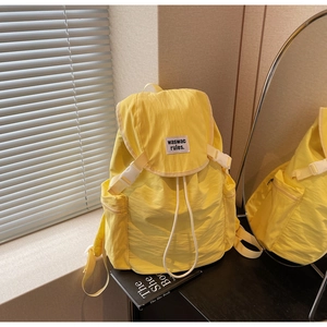 Detail of yellow nylon backpack featuring flap drawstring closure and side pocket detail