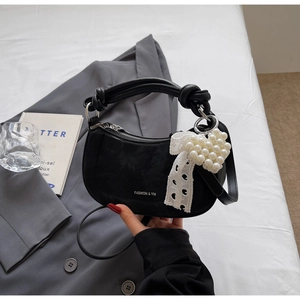 Detail of black crescent handbag featuring a white lace bow and pearl heart charm