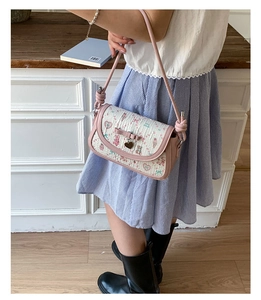 Close-up of pink shoulder bag featuring cartoon prints, a bow and heart pendant charm