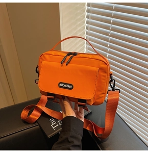 Detail of a bright orange nylon crossbody bag with dual zippers and brand logo