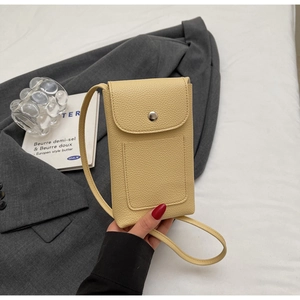 Détail d'un petit sac de téléphone en cuir grainé jaune pâle posé sur un blazer gris