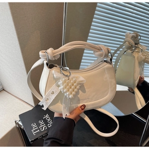 Detail of white patent leather half-moon bag featuring knot handle and pearl heart charm
