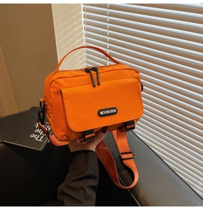 Detail of orange messenger bag with Moonlersa logo, top handle and nylon texture