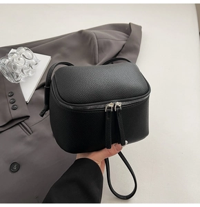 Detailaufnahme einer schwarzen Mini-Umhängetasche aus Leder mit Litschi-Struktur und Reißverschluss