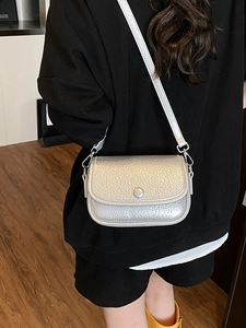 Silver pebble textured crossbody bag with flap and metal buckle on back of model