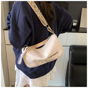 Détail d'un sac demi-lune crème avec large bandoulière jacquard porté par un mannequin