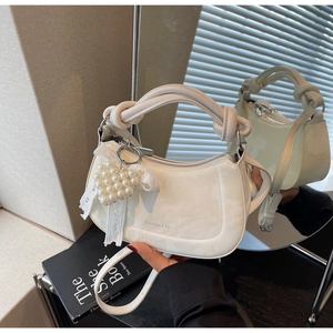 Macro detail of creamy handbag featuring a knotted handle and a heart pearl lace charm