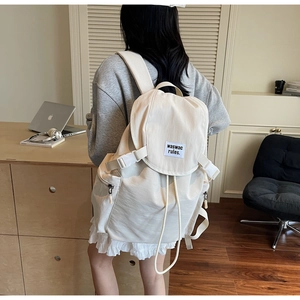 Detailed back view of a cream canvas backpack worn in a cozy indoor lifestyle setting