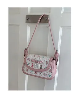 Detail of pink ballet-style crossbody bag featuring cartoon prints and heart pendant