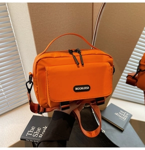 Detail of bright orange nylon crossbody bag with buckle front pocket and adjustable strap