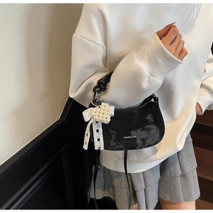 Detail of black glossy hobo bag with pearl heart charm and ribbon on model