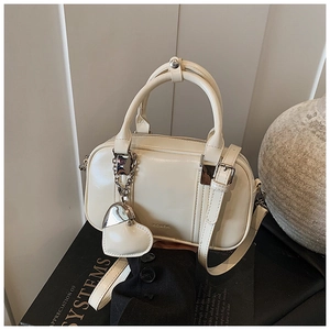 Detail of cream Boston bag with heart pendant and adjustable strap on a minimalist decor