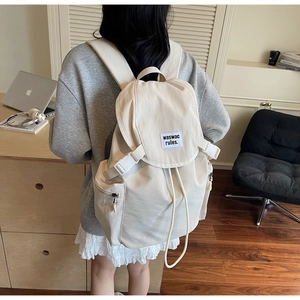 Rear view of a model wearing the cream canvas backpack with flap closure and woven label