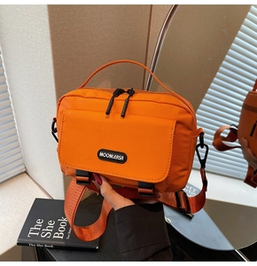 Detail of orange nylon messenger bag with double zippers and black logo on a book