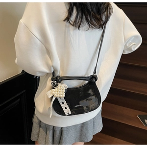Detail of glossy black crescent crossbody bag with pearl bow and fashion branding