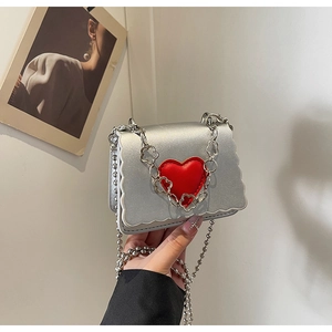 Detail of silver wavy-edge mini bag featuring a 3D red heart and floral metal chain