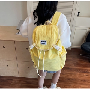 Detail of yellow nylon backpack featuring white buckle closure and brand label decoration