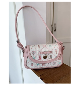Close-up of pink crossbody bag with cartoon prints, bow decoration and heart pendant