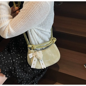 Detail of light green half-moon bag featuring knot strap and lace bow with pearl charm