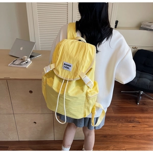 Rear view of a model wearing the yellow nylon backpack with drawstring and flap closure