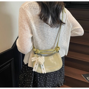 Detail of avocado green crescent bag with pearl heart pendant and lace bow on wooden stairs