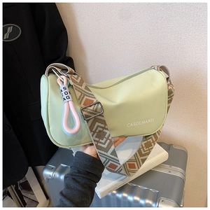 Détail d'un sac bandoulière vert clair avec sangle large à motifs sur une valise argentée