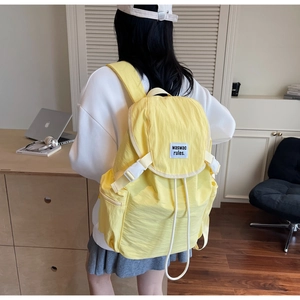 Detail view of the yellow canvas backpack showing the side zipper pocket and snap buckle