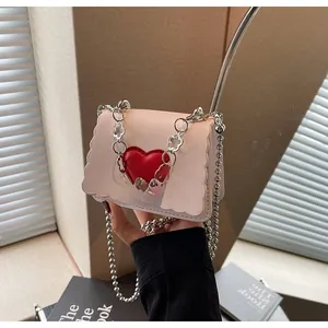 Detail of light beige mini bag featuring scalloped edges and a red heart ornament