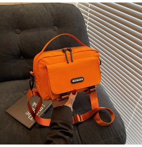 Detail of orange nylon crossbody bag with dual buckles and woven shoulder strap