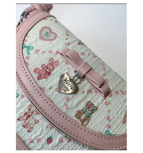 Detail of pink bow and heart metal tag on patterned crossbody bag with bear print