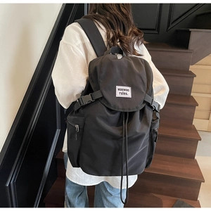 Close-up of black nylon backpack featuring flap closure and functional side zip pockets