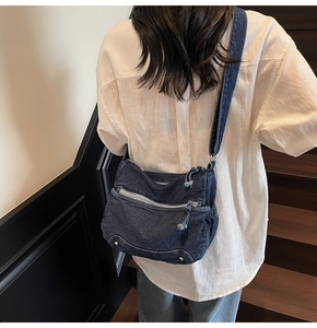 Detail of dark blue denim tote bag with metal studs and multiple zipper pockets