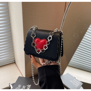 Detail of a mini black crossbody bag with a 3D red heart and silver flower chain decoration