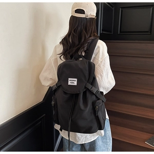 Rear view of a model wearing a large black canvas backpack with flap and buckle closure
