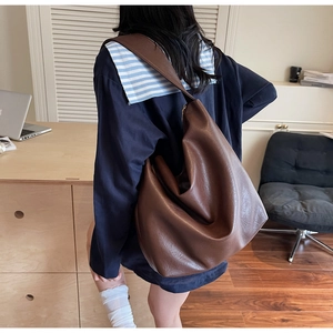 Detail of soft brown PU leather tote bag with wide strap on model in indoor office setting