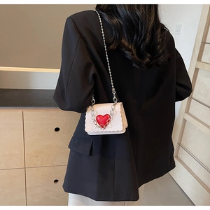 Close-up of a white mini chain bag with a red heart and wavy edge detail worn over a black blazer
